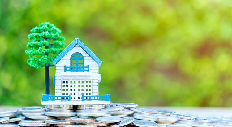 A model house is sitting on top of a pile of coins.