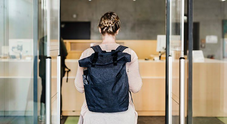 A woman with a backpack is standing in front of a glass door.