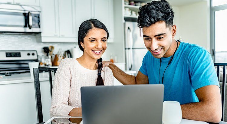 A man and a woman are sitting at a table looking at a laptop computer.