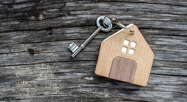 A wooden house keychain with a key on a wooden table.
