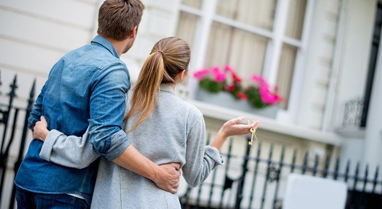 A man and a woman are standing in front of a house holding keys.