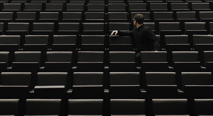 A man in a black suit is standing in an empty auditorium.