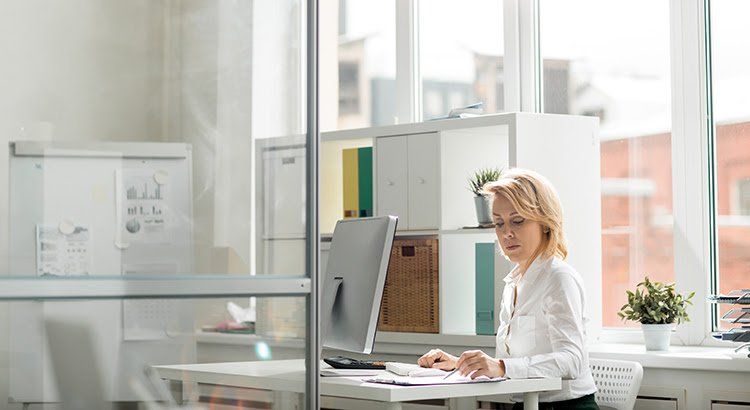 A woman is sitting at a desk in front of a computer in an office.