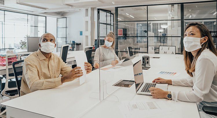A group of people wearing face masks are sitting at a table in an office.