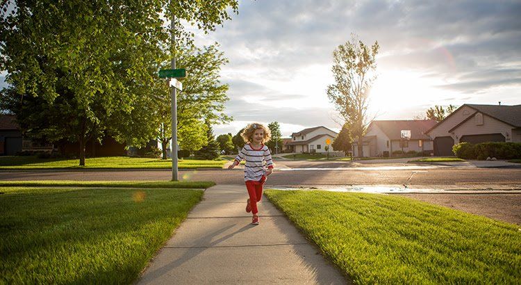 A little girl is running down a sidewalk in a residential neighborhood.