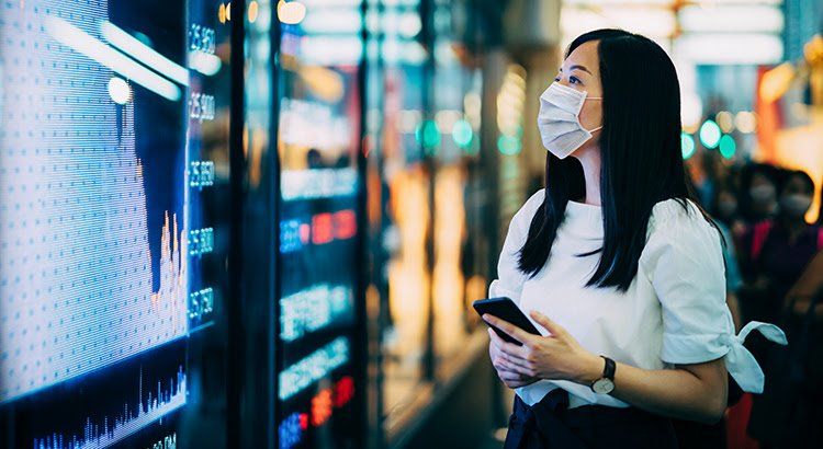 A woman wearing a face mask is looking at a screen while holding a cell phone.