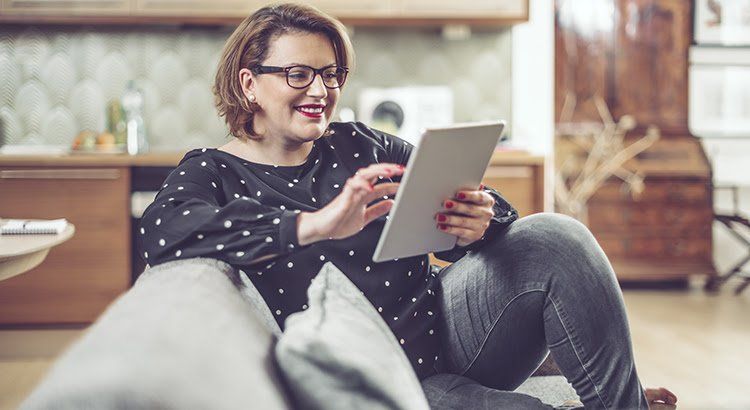 A woman is sitting on a couch using a tablet computer.