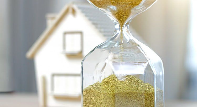A hourglass with sand pouring out of it in front of a model house.