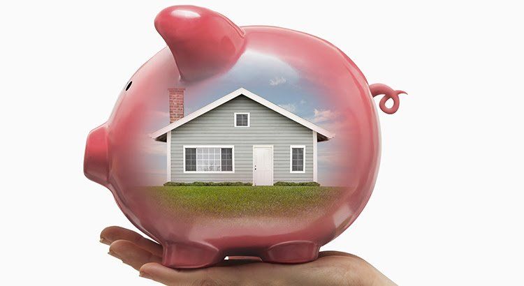 A person is holding a pink piggy bank with a house inside of it.