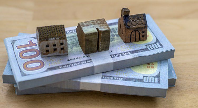 A stack of money with three small houses on top of it.