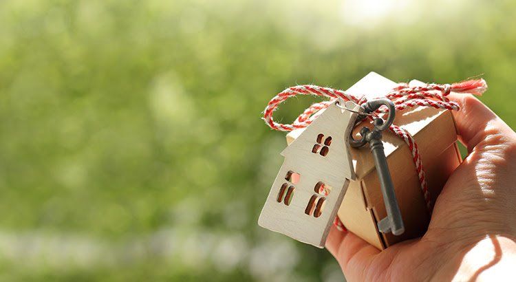 A person is holding a wooden house and a key.