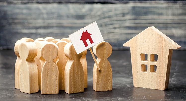 A group of wooden people holding a sign with a house on it.