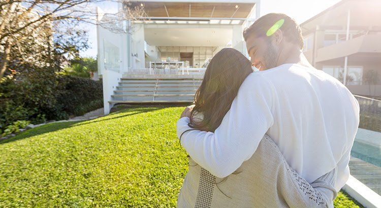A man and a woman are hugging in front of a house.