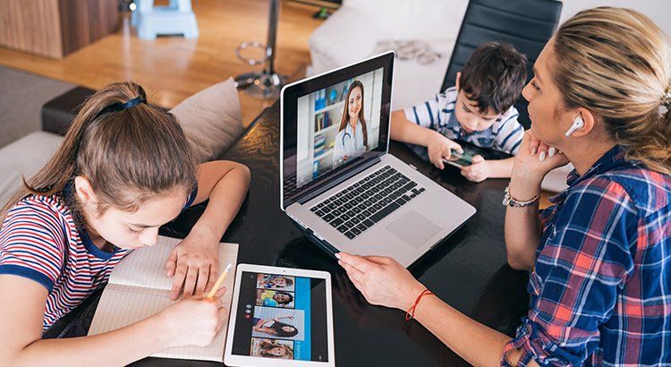 A woman and two children are sitting at a table with laptops and tablets.