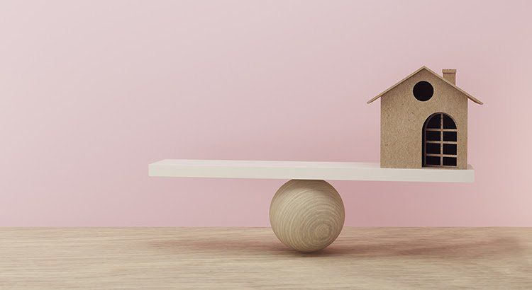 A small house is sitting on top of a wooden ball on a seesaw.