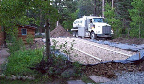 Septic truck parked near a new leach field, beside a wooden building in a wooded area.