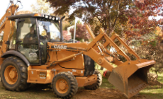 Orange Case backhoe in a yard. Operator visible inside cab.