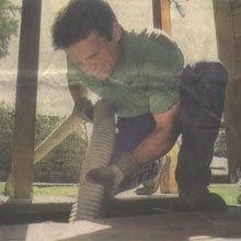 Man in green shirt and gloves kneeling, holding hose, likely for construction or cleaning.