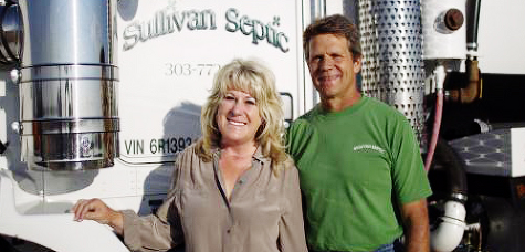 Two people smiling in front of a Sullivan Septic truck. One wears a green shirt, the other a tan blouse.