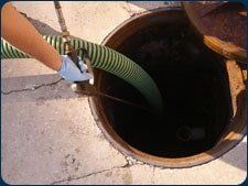 Hand with hose emptying contents from an open septic tank.