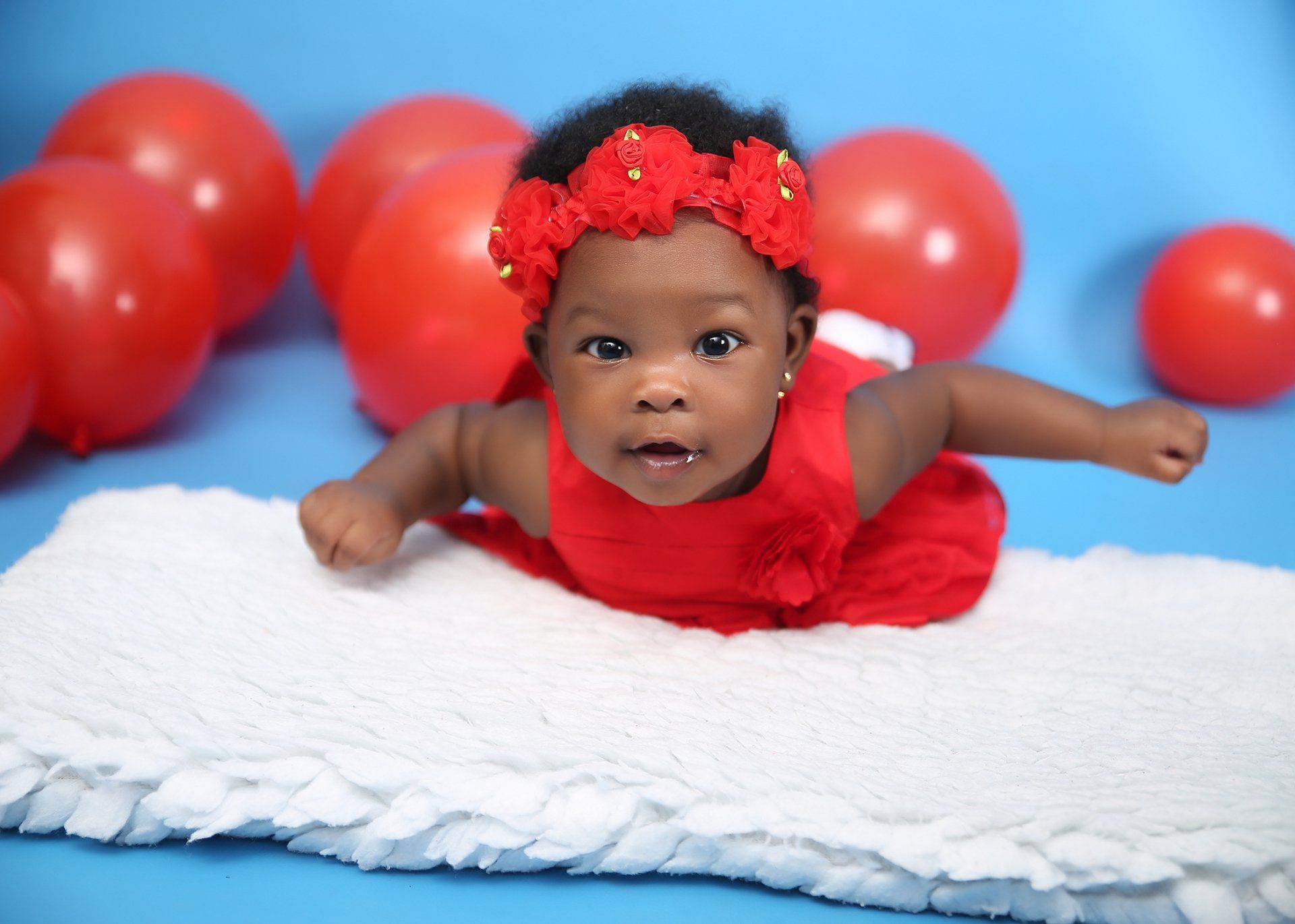 The baby is wearing a red dress and a red headband.
