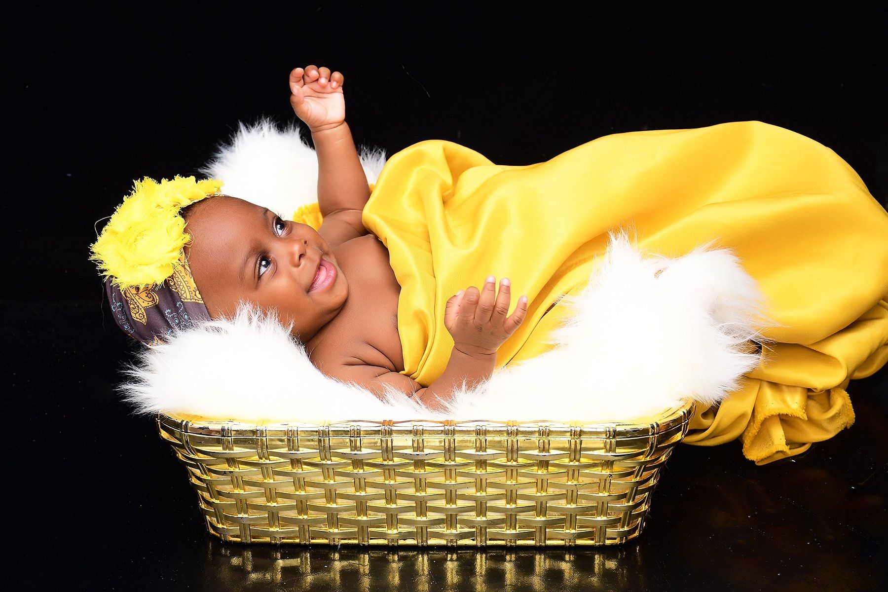 A baby wrapped in a yellow blanket is laying in a basket.