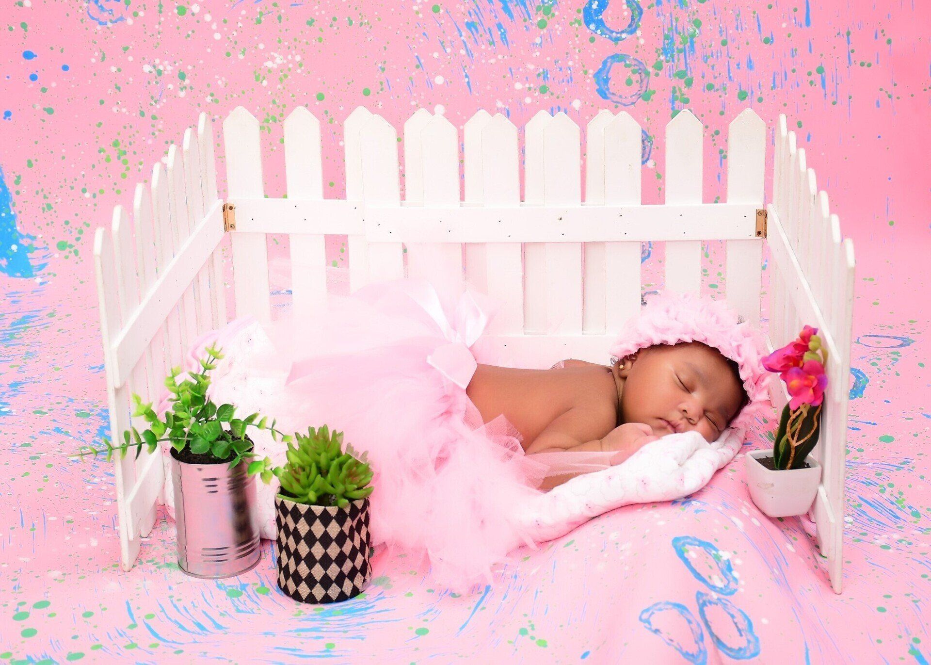 A baby is sleeping in a pink crib with a white fence.