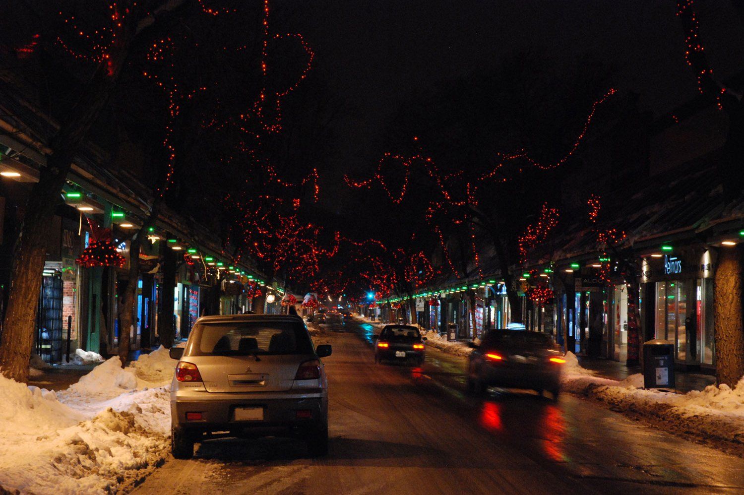 A car is parked on the side of a snowy street at night.