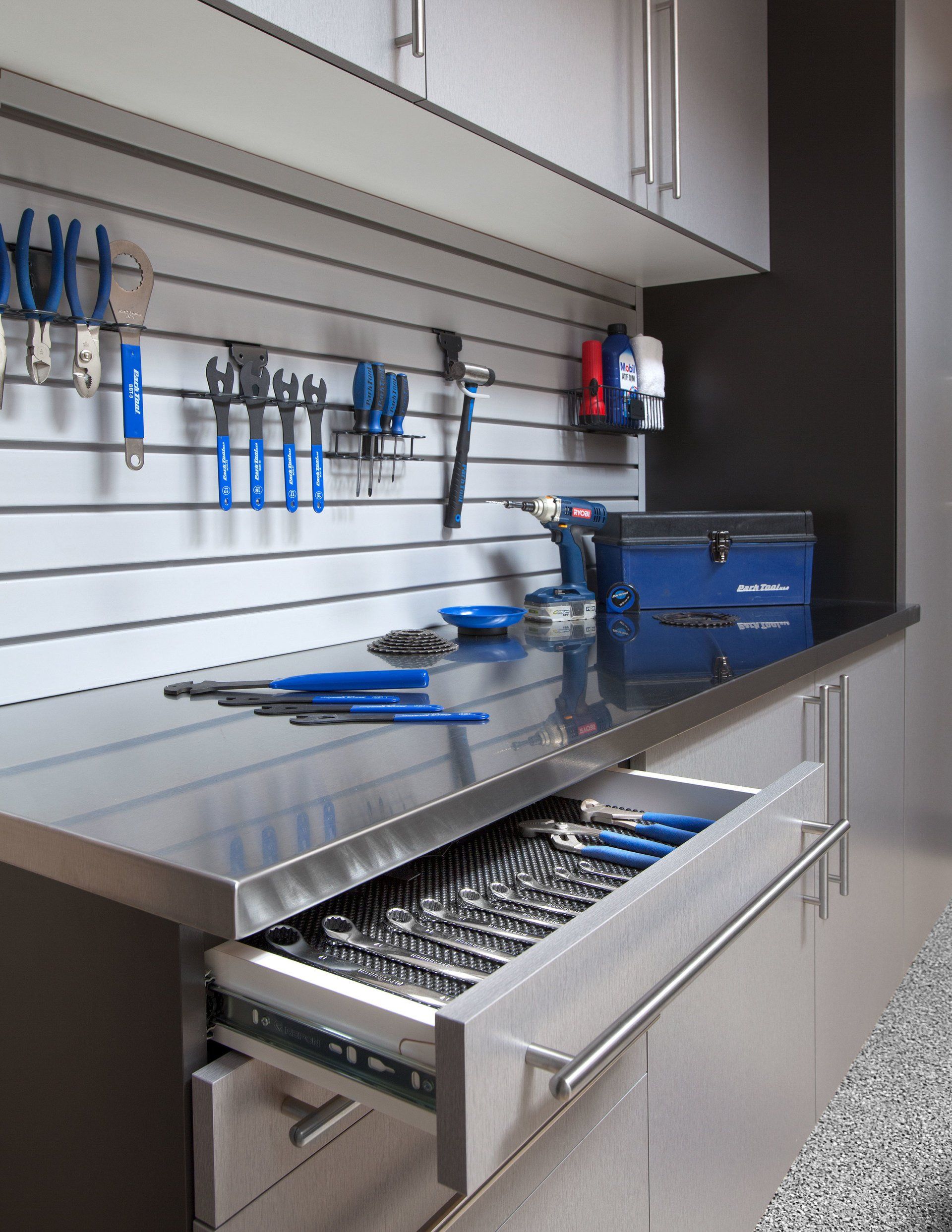 A modern garage workshop featuring a stainless steel workbench, wall-mounted tool organizers, and an open drawer.