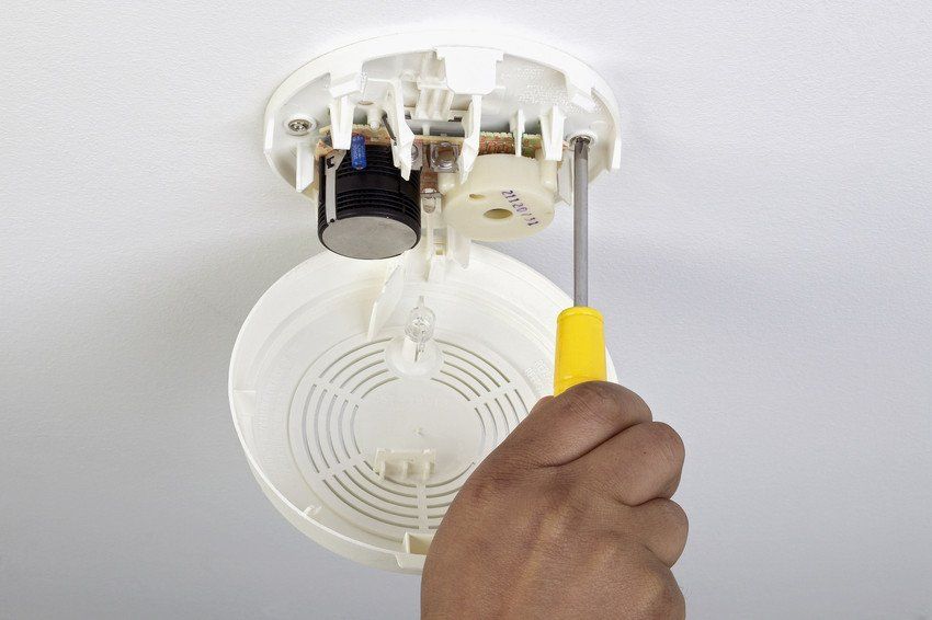 An engineer fixes a smoke detector to the ceiling