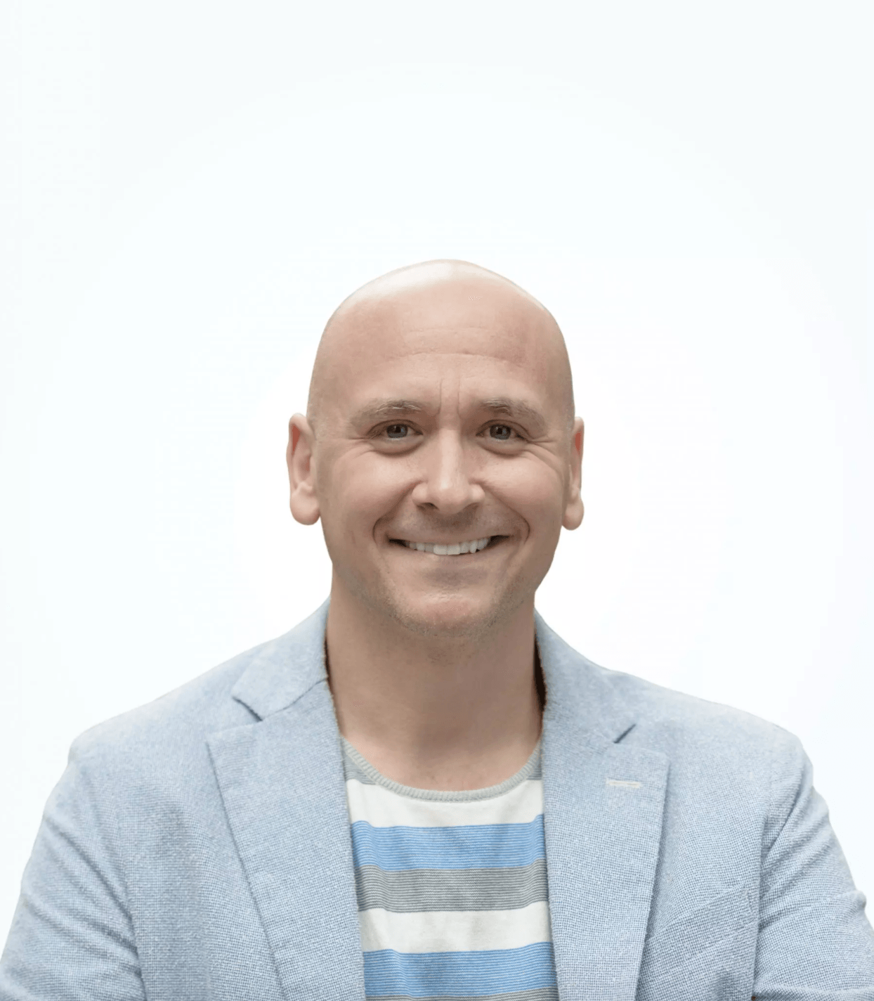 A bald man wearing a blue jacket and striped shirt smiles for the camera