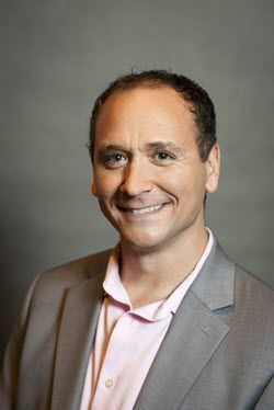 A man in a suit and pink shirt is smiling for the camera.