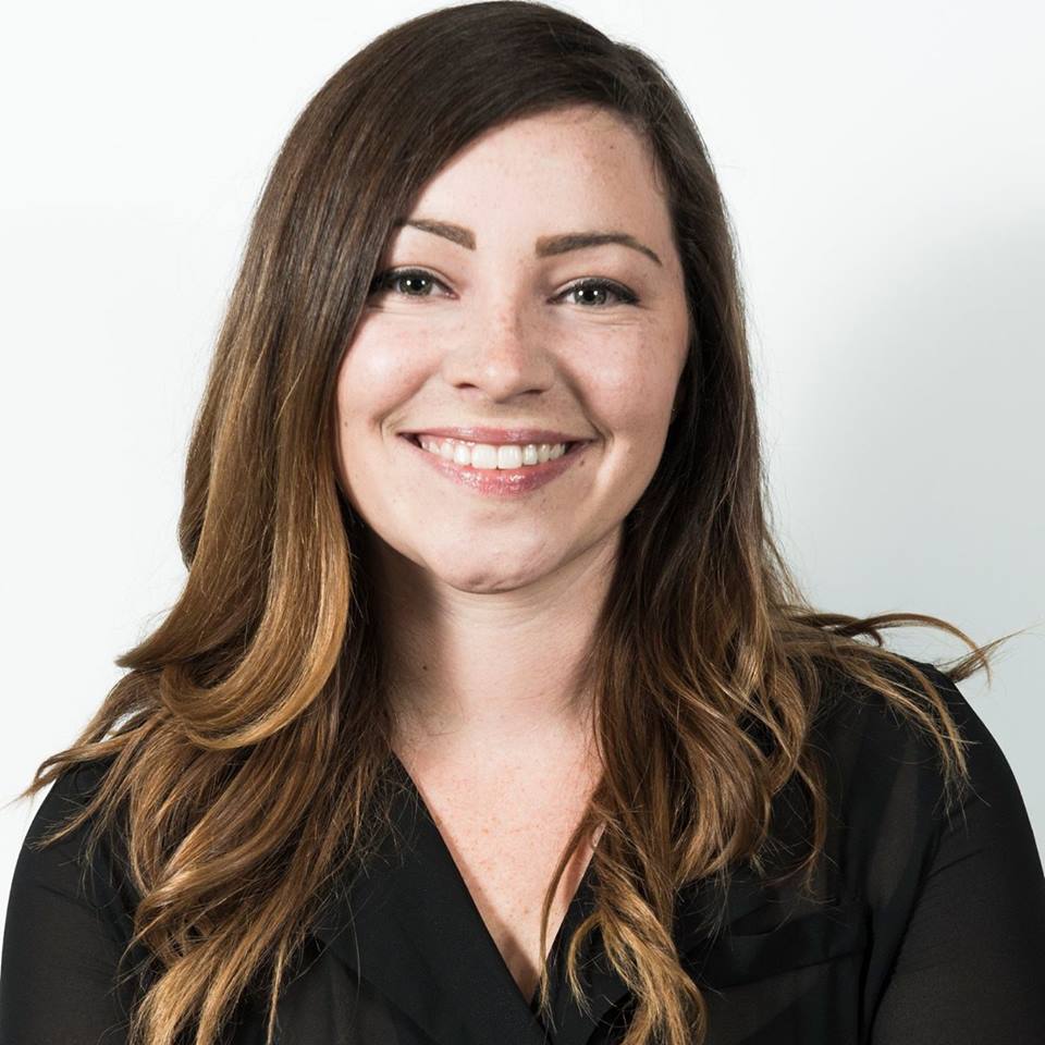 A woman with long brown hair is smiling and wearing a black shirt.