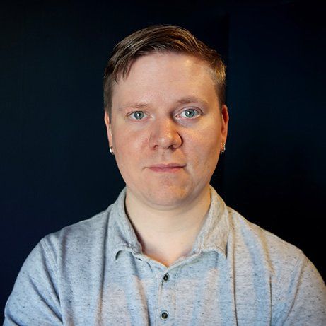A man in a grey shirt is looking at the camera.