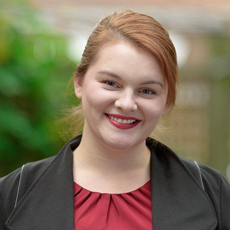 A woman wearing a red shirt and a black jacket is smiling for the camera.