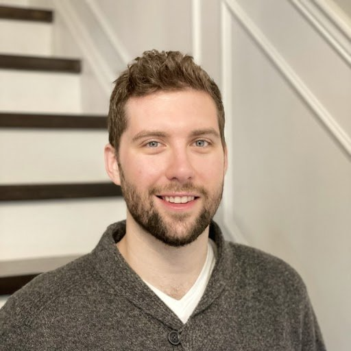 A man with a beard is smiling in front of a set of stairs.