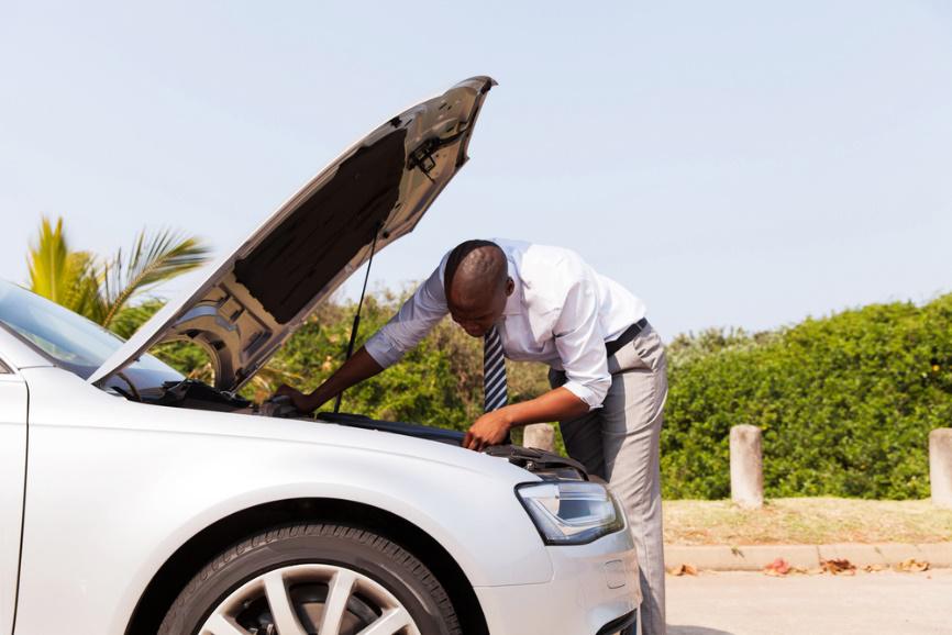 A man is looking under the hood of a broken down car.