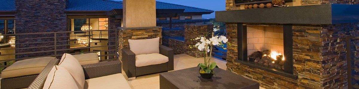 Modern stone patio with outdoor fireplace, lounge chairs, and warm evening lighting
