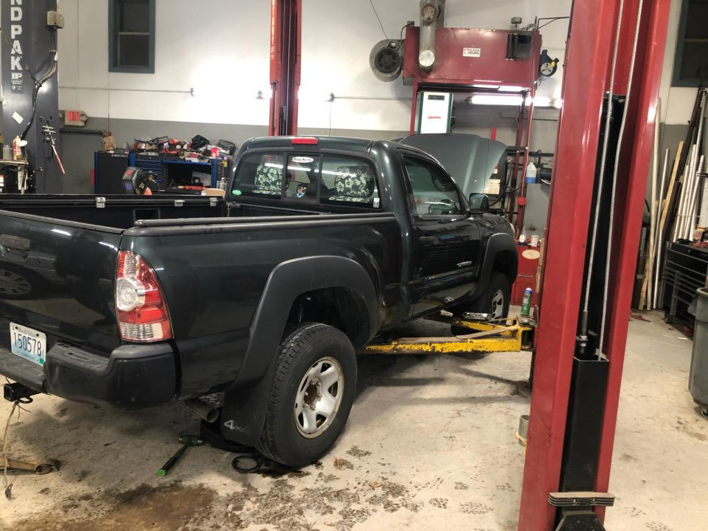 Black pickup truck on a lift in an auto repair shop, with the driver door open.