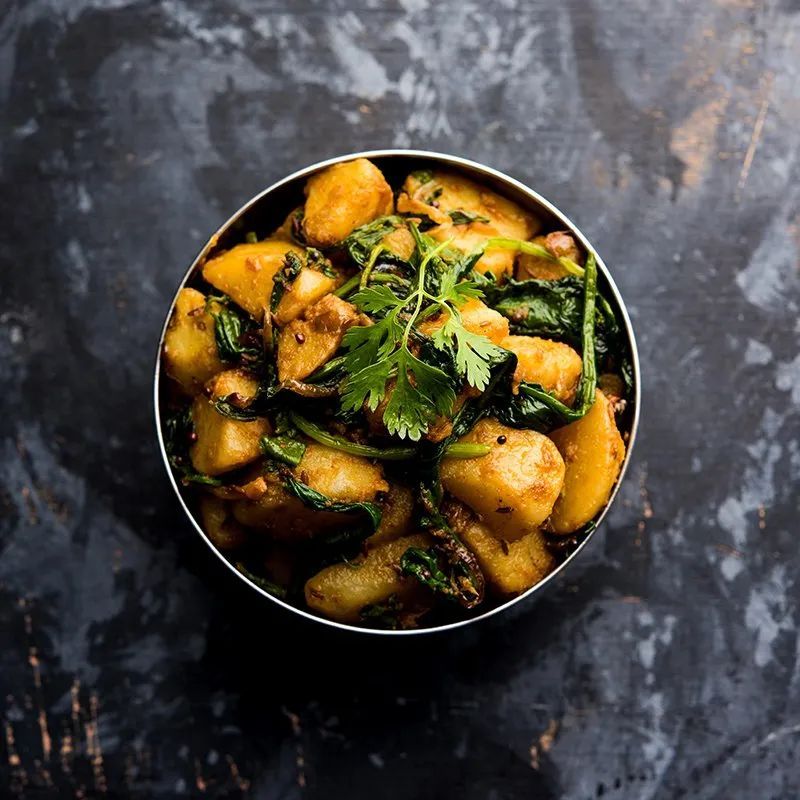 A bowl of potatoes and spinach on a table.