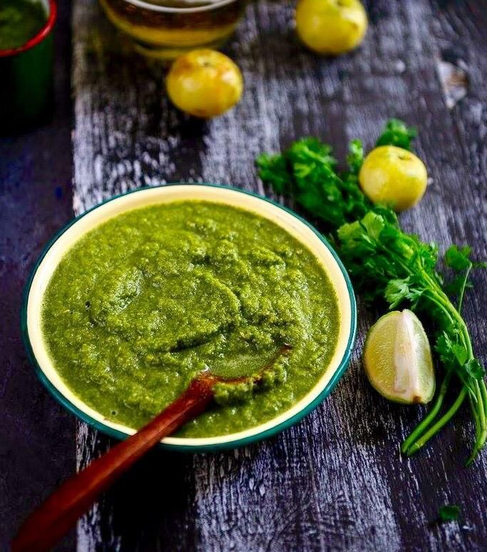 A bowl of green sauce with a wooden spoon in it on a wooden table.