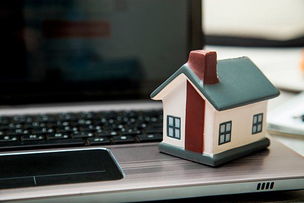 A small ceramic home sits on top of an open laptop computer.