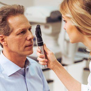 A woman is examining a man 's eyes with an ophthalmoscope.