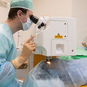 A surgeon is looking through a microscope at a patient.