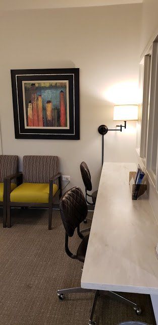 A waiting room with chairs , a desk , and a painting on the wall.