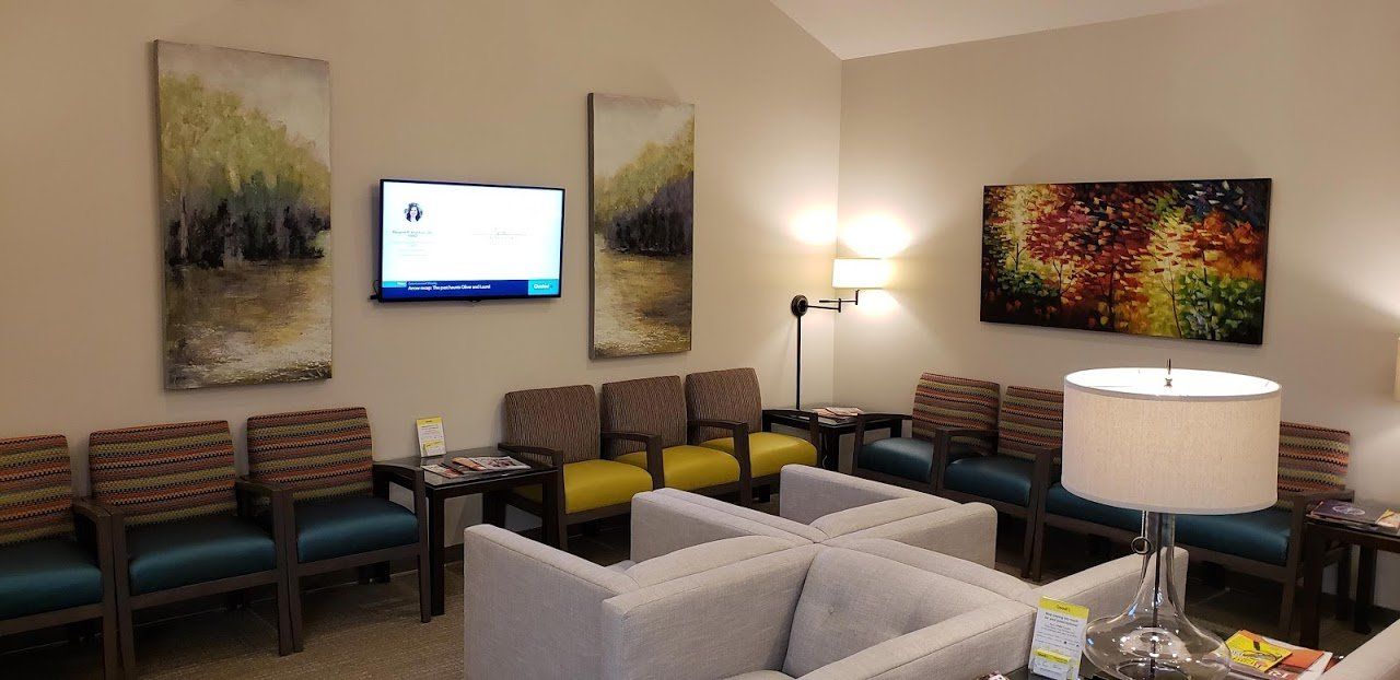 A waiting room with a couch , chairs and a flat screen tv.
