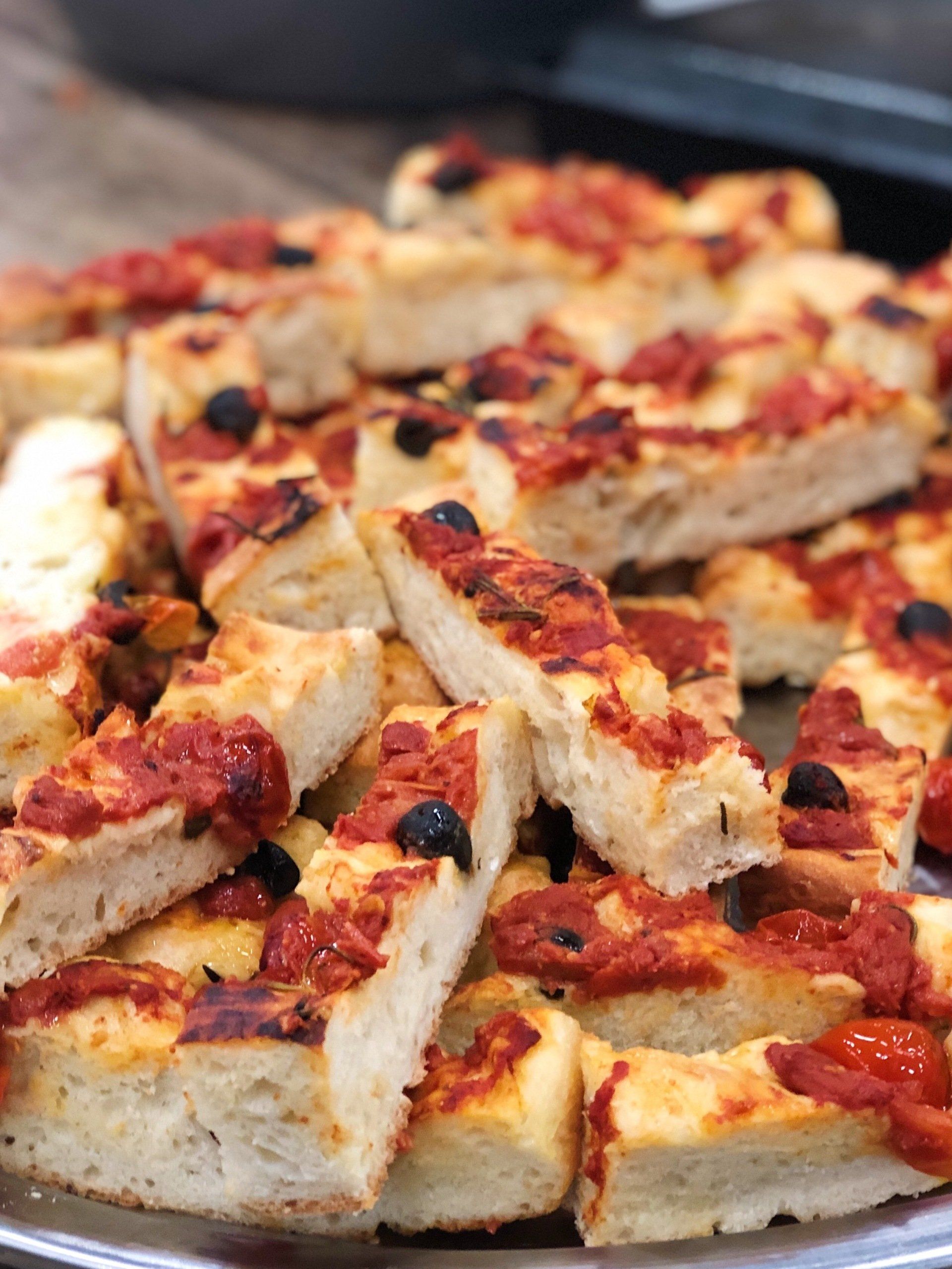 Sliced focaccia with tomatoes and olives browned crust edges, catering menu for a corporate event in Amsterdam
