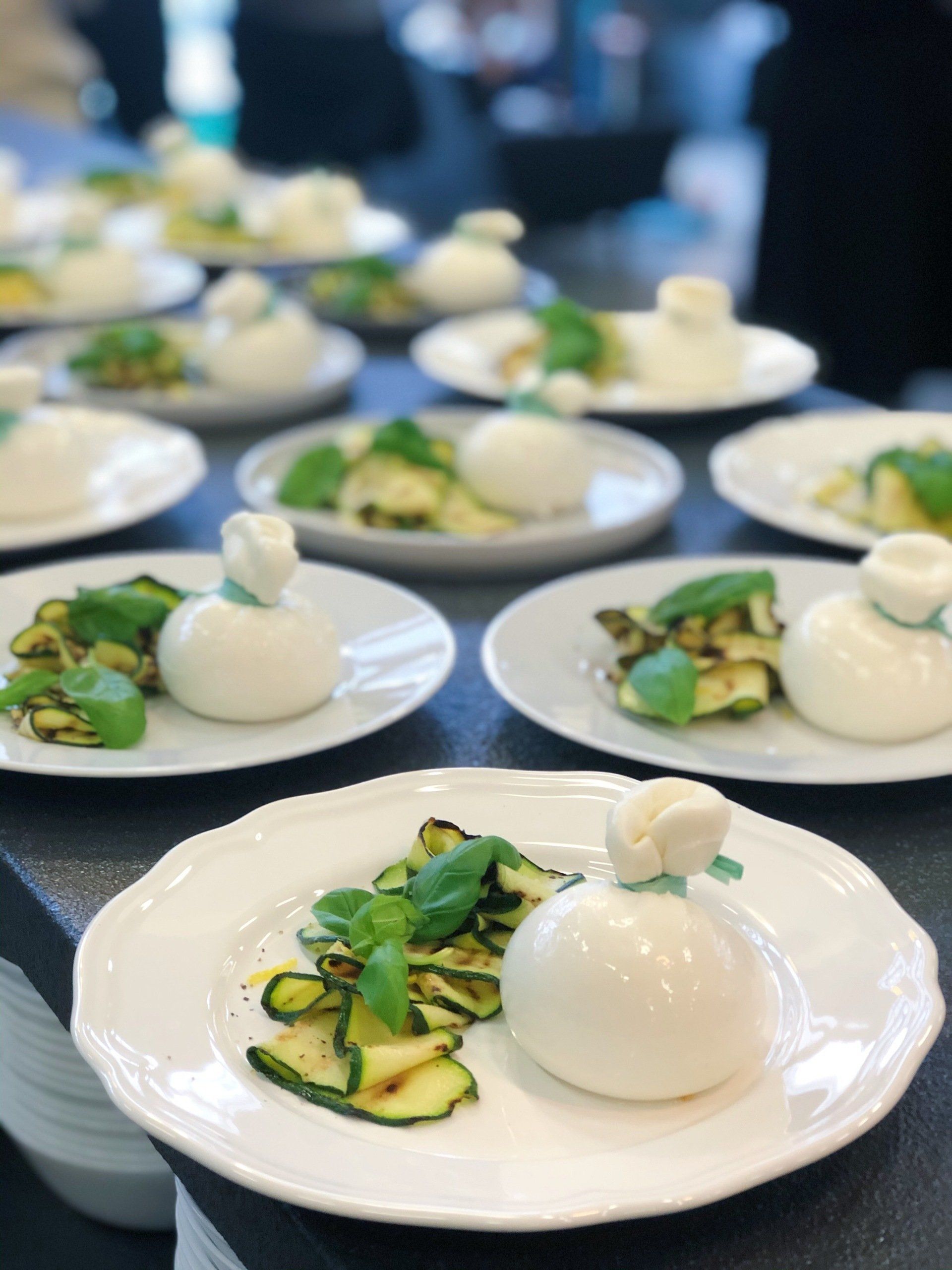 Plated burrata with zucchini and basil arranged in rows on a dark tablecloth, catering for a private event