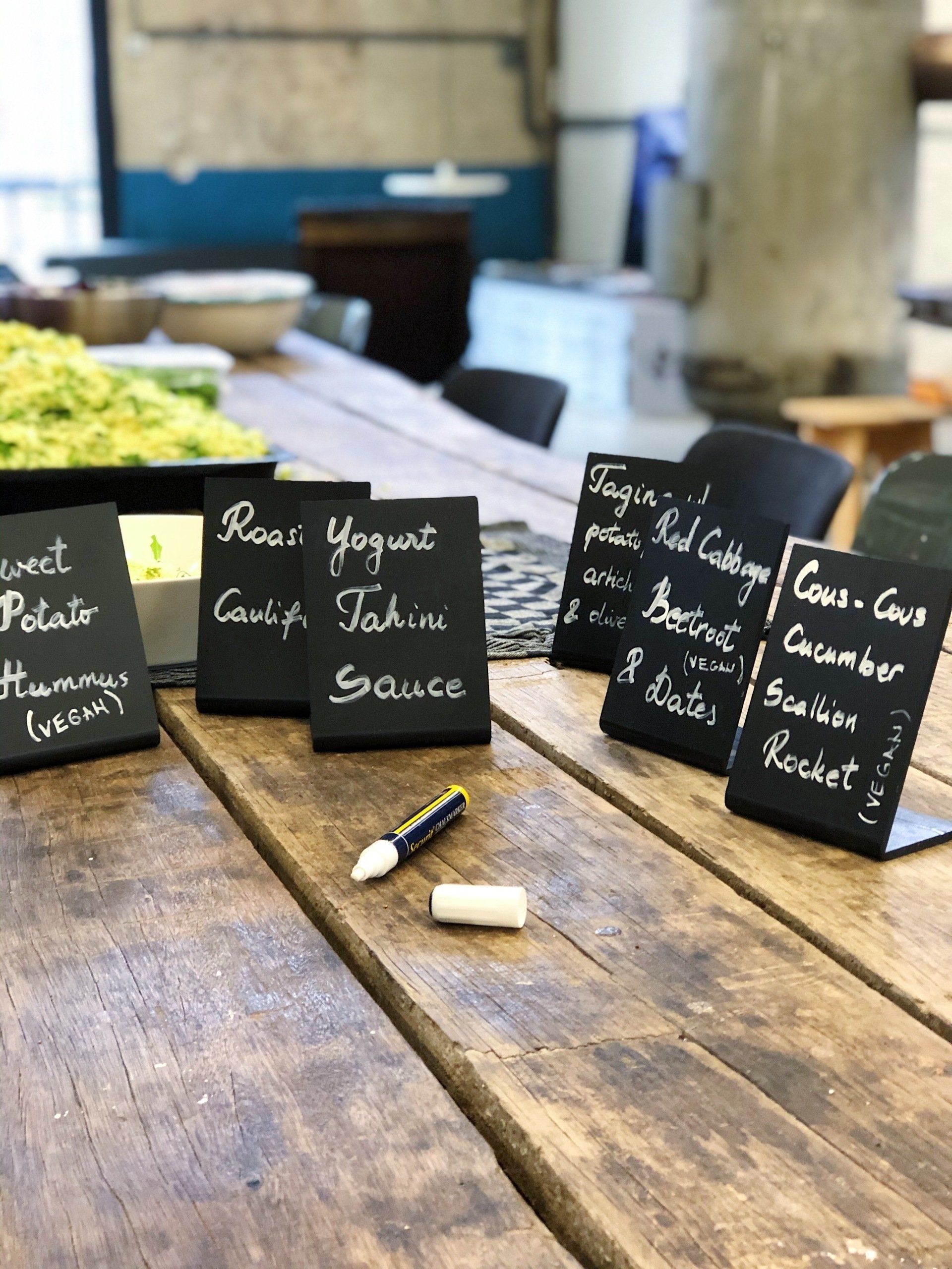 Chalkboard menu signs on a rustic wooden table in a café, with chalk sticks in front