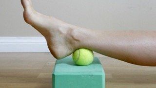 A person is using a tennis ball to massage their ankle.